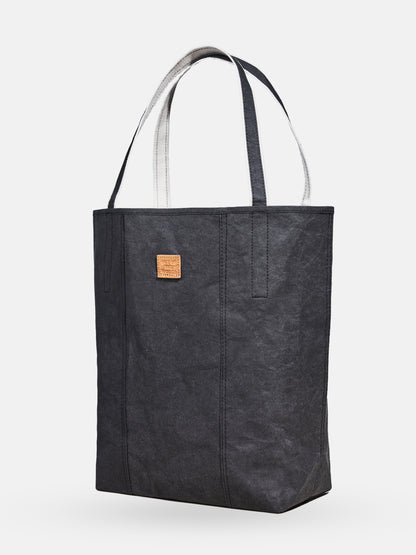 Black shopper tote bag with dual handles and small leather patch on neutral background