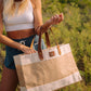 Woman holding a large jute tote bag with leather handles outdoors in a sunny natural setting