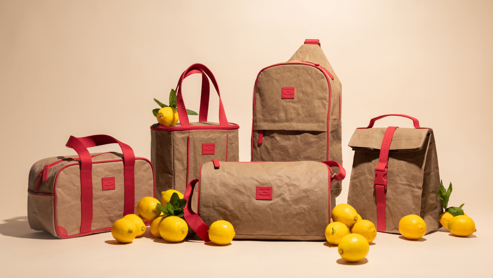 Set of stylish beige and red bags displayed with fresh lemons on a neutral background