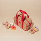 On the Move Lunch Cooler with red straps and zipper, surrounded by colorful sprinkled donuts on beige background