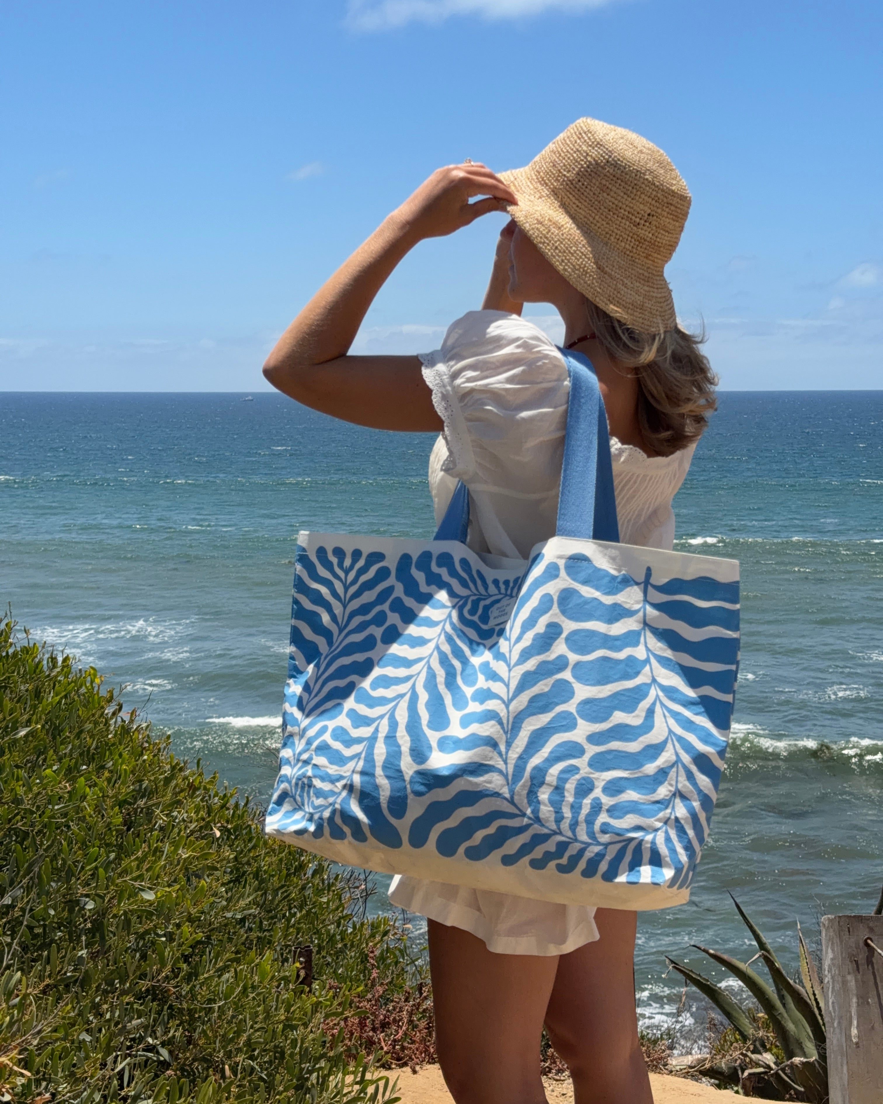 A woman wearing a beachy printed analog tote on a summer day in a coastal setting.