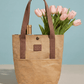 beige tote bag with chestnut colored handles containing a bottle of wine and a bouquet of pink tulips