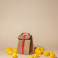 Paper Sack Lunch Cooler with fold-top and buckle, insulated reusable bag surrounded by fresh lemons on beige background