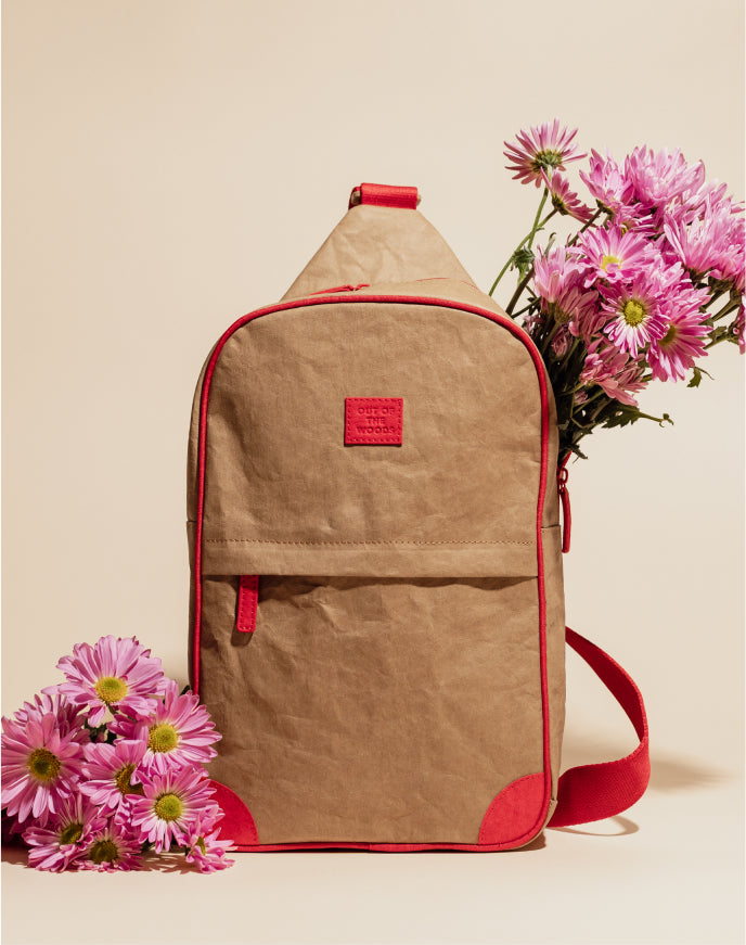 Minimalist brown sling bag with red accents surrounded by pink flowers on neutral background