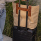 Jute T-Strap Tote secured on a black wheeled suitcase with leather handles and rivets for travel convenience.