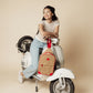 Young woman leaning on white scooter with a Zip Around Sling backpack hanging on the handlebar, casual and confident style